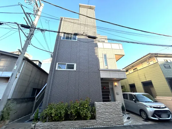 落ち着いた色合いの外壁とモダンなデザインが印象的な外観です。敷地内には駐車スペースや植栽が配置され、住まいの顔としての機能性と美観を兼ね備えています。