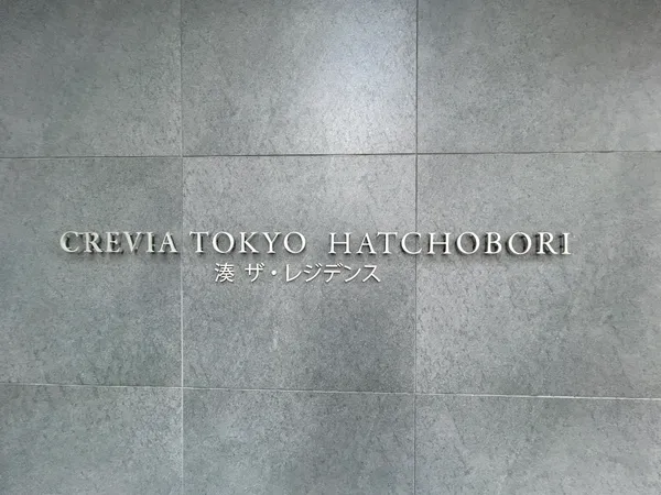 物件名「CREVIA TOKYO HATCHOBORI 湊 ザ・レジデンス」のエントランスサインです。シンプルなグレー系タイル壁に、立体的なロゴが映えるデザインとなっています。