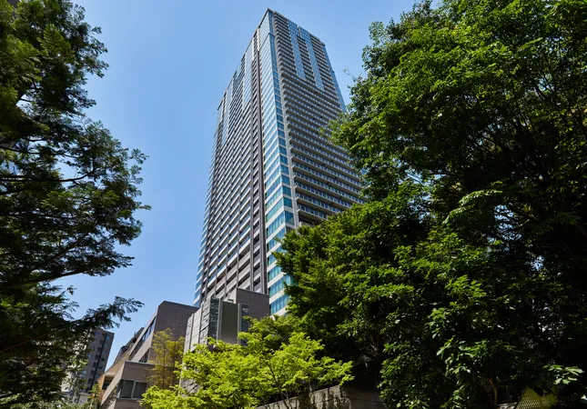 マンションの外観写真です。周囲には豊かな緑が広がり、建物の高さと開放感が印象的です。晴れた空と調和したガラス面が、明るく清潔感のある雰囲気を演出しています。