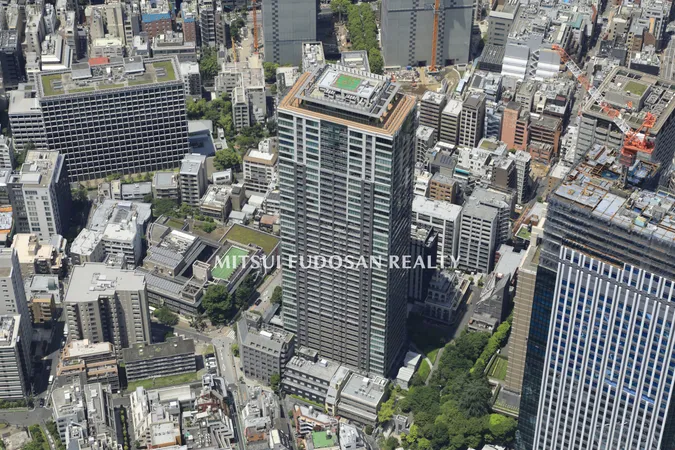 マンションの外観写真です。周囲には豊かな緑が広がり、建物の高さと開放感が印象的です。晴れた空と調和したガラス面が、明るく清潔感のある雰囲気を演出しています。
