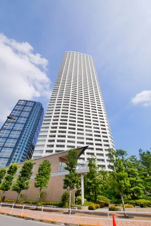 白を基調とした高層マンションの外観。広いバルコニーと植栽が特徴的です。