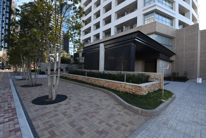 エントランス前には植栽と広い歩道が整備され、建物外観は現代的なデザインです。