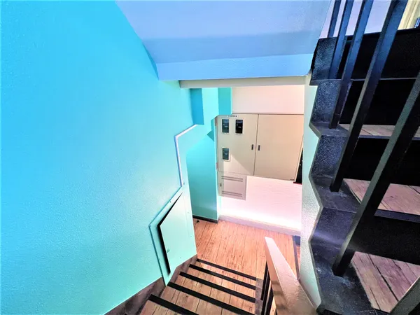 共用階段の様子です。明るいブルーの壁と木目調の床材が特徴的で、清潔感のある印象です。階段はしっかりとした造りで、手すりも設置されています。