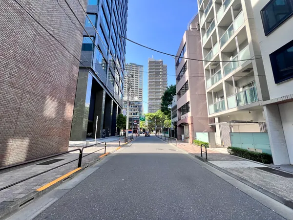 周辺の街並みの写真です。幅の広い道路に面し、両側には高層マンションやオフィスビルが立ち並んでいます。緑も点在しており、都市的な利便性と快適な生活環境が両立されたエリアであることがうかがえます。