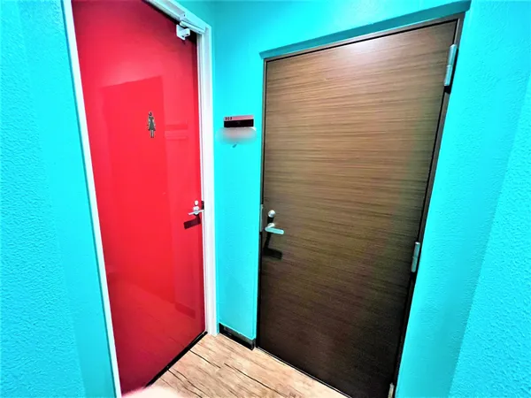 写真は共用部の廊下に面した2つのドアが並ぶ様子です。壁は鮮やかな水色で、床は木目調のデザインです。