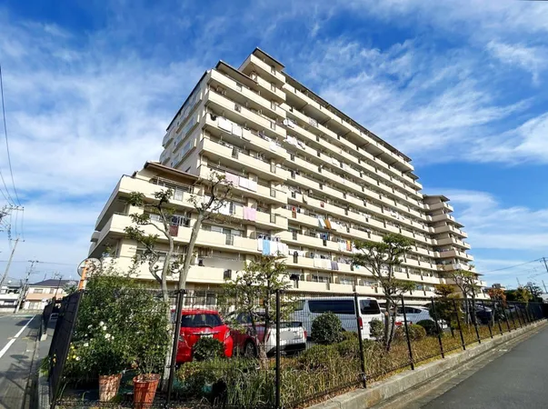 南向きバルコニーが並ぶ大型マンション。敷地内に駐車場と植栽が整備されています。