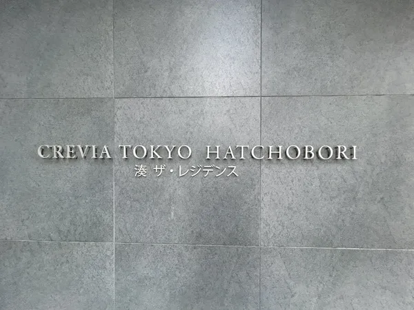 物件名「CREVIA TOKYO HATCHOBORI 湊 ザ・レジデンス」のエントランスサインです。シンプルなグレー系タイル壁に、立体的なロゴが映えるデザインとなっています。