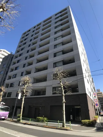 物件の外観写真です。タイル貼りのファサードが特徴的で、バルコニーが各住戸に設けられています。大通りに面しており、周辺には植栽や歩道が整備されています。