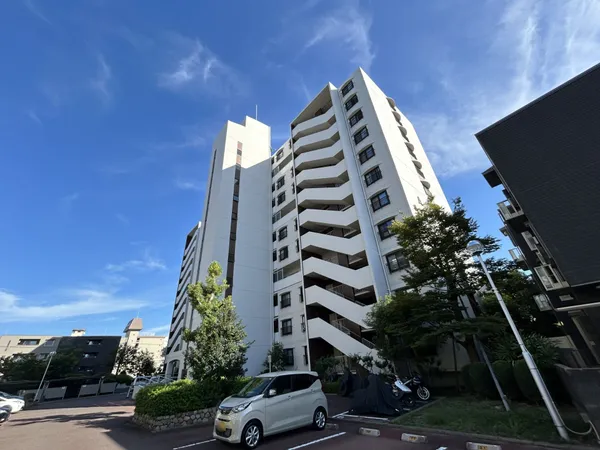 白を基調とした外観のマンション。敷地内駐車場や緑があり、開放的な印象です。