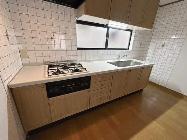 キッチンです。キッチン台は壁付けタイプのシステムキッチンが採用されています。収納スペースが豊富なため、すっきりと片付いた空間を保つのに役立ちそうです。