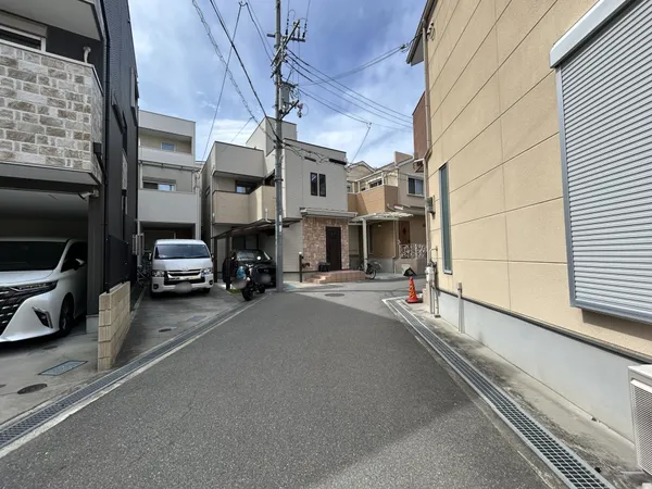道幅は車のすれ違いが可能な広さで、周囲には駐車スペースやガレージ付きの戸建が並んでいます。玄関前の段差やアプローチもゆとりがあり、来客時や日常の出入りがしやすい環境です。
