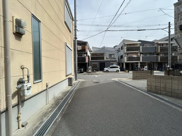 幅員が十分にあり、車の出入りや歩行者の通行がしやすい印象です。周囲は住宅が並び、落ち着いた雰囲気の街並みが広がっています。道路沿いの視界が抜けており、日中は明るさを感じられる環境です。