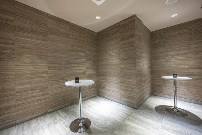 過熱式タバコが喫煙できるシガールーム。落ち着いた色調の壁と床でまとめられ、スタンディングテーブルが設置されています。分煙対策が施された空間で、喫煙者も安心して利用できる共用設備です