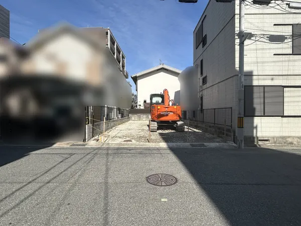 道路に面した敷地の写真です。幅員のある前面道路に接しており、車両の出入りや来客時の案内がしやすい印象です。両側には住宅が建ち並び、落ち着いた住環境が期待できそうです。