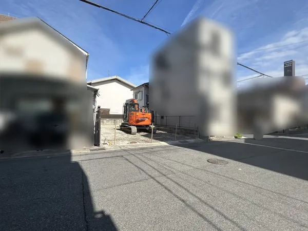 道路に面した敷地の写真です。幅員のある前面道路に接しており、車両の出入りや来客時の案内がしやすい印象です。両側には住宅が建ち並び、落ち着いた住環境が期待できそうです。