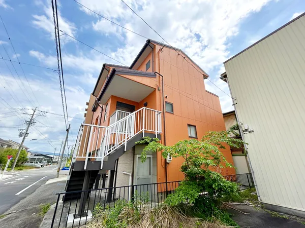 外階段と白い手すりがアクセントとなり、道路からの視認性も良好です。前面道路は幅が広く、車や自転車の出入りもしやすい環境です。