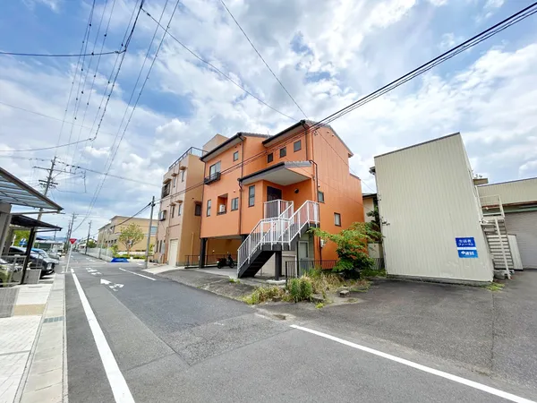 建物前面には階段付きのエントランスがあり、道路からのアクセスがしやすい構造です。周囲は幅のある道路と駐車スペースが広がり、車の出入りや来客時にも便利な環境です。