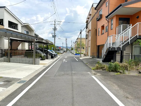 幅員がしっかりと確保された前面道路の様子です。両側に住宅や駐車場が整然と並び、車の出入りや歩行者の通行も安心できる環境です。