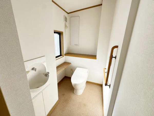 窓付きで明るいトイレ。手洗いカウンターと手すりが設置されています。