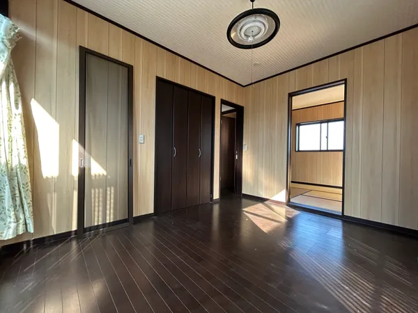 【洋室 約6.0帖】木目調の壁が温もりを演出する洋室。大きな窓から光が差し込み、収納充実で快適に過ごせる空間です。