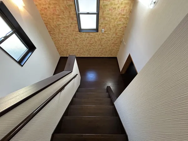 【階段】明るい窓から光が差し込む階段スペース。手すり付きで安心、壁のアクセントが空間に温もりを添えています。