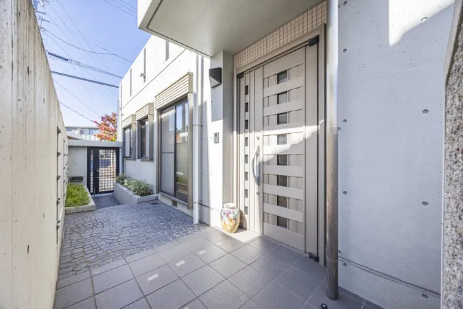 コンクリート壁とタイル床の玄関アプローチ。門扉から玄関まで直線的な動線で、明るい印象です。