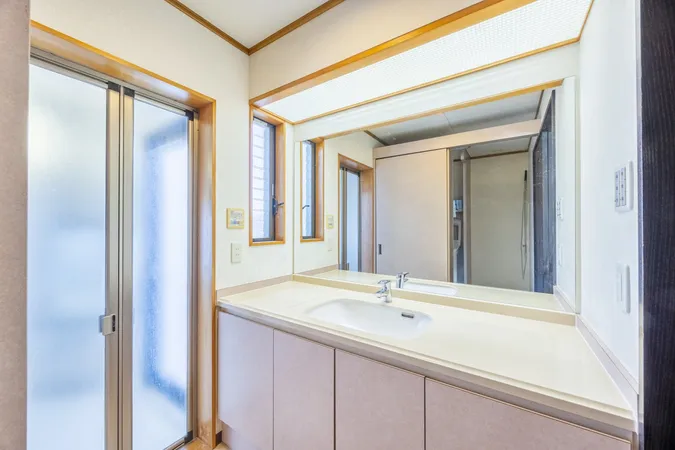 広めのカウンターと大型ミラーを備えた洗面スペース。窓から自然光が入り、収納スペースも充実しています。